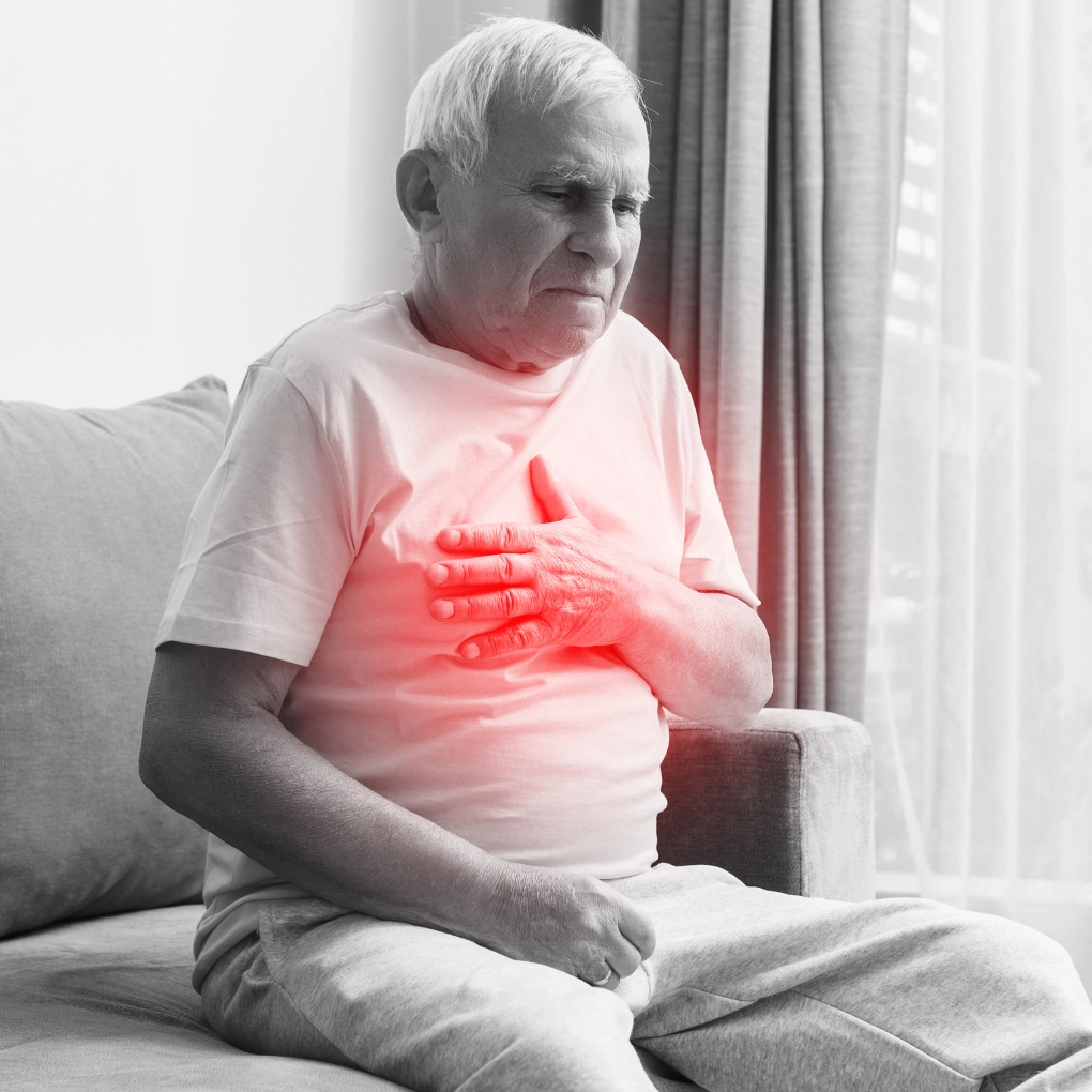 A black and white image of an elderly man sitting on a couch holding his chest Due to pain his lungs (ILD).